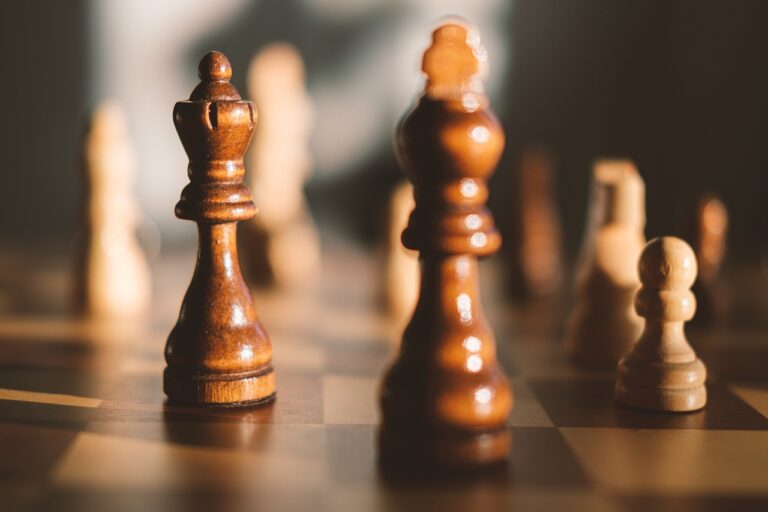 Chess pieces on a chess board, in the middle of a game and with the black king and queen as well as white knight and pawn in focus, meant to signify strategy.